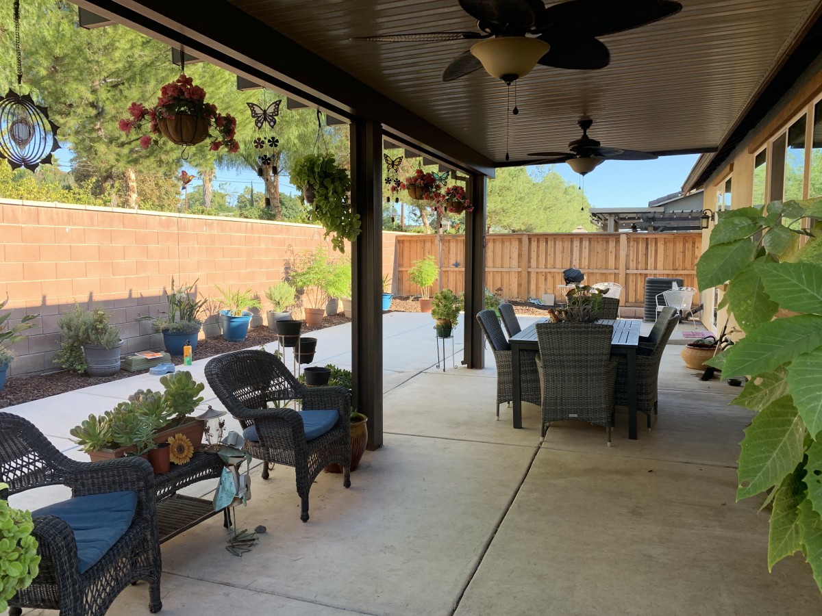 A cozy patio with outdoor seating and a dining area, surrounded by plants and hanging baskets.