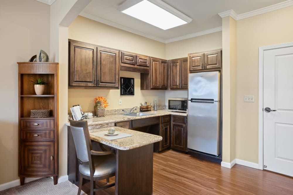 A modern kitchen with wooden cabinets and flooring, featuring a refrigerator and small dining area.