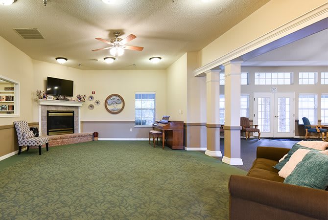 A cozy living room featuring a fireplace, ceiling fan, and various seating areas with a television mounted on the wall.