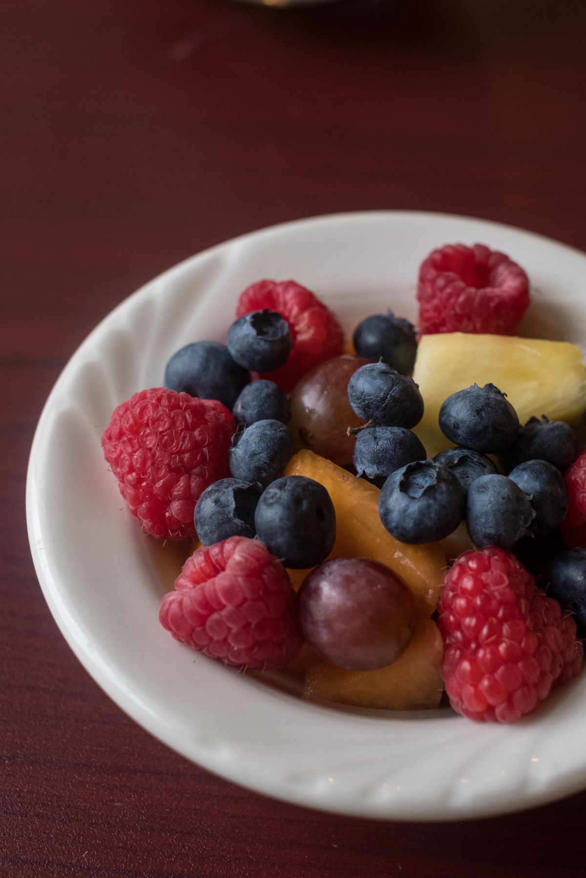 A bowl filled with fresh raspberries, blueberries, grapes, and pineapple pieces.