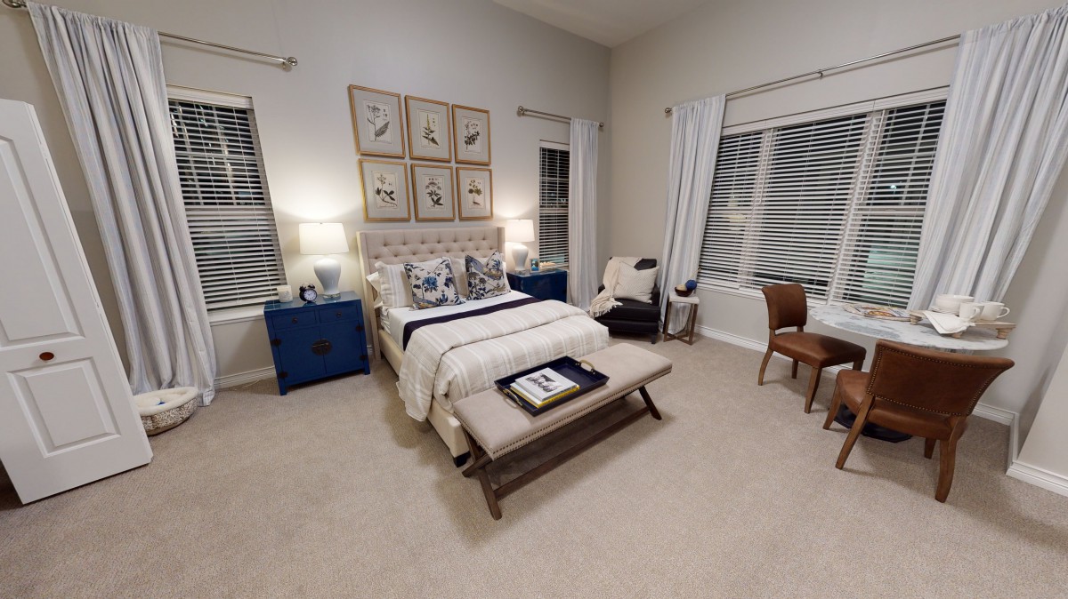 A cozy, well-decorated bedroom with a neatly arranged bed, artwork on the wall, and warm lighting.