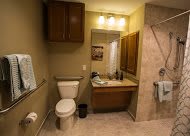 A well-lit bathroom with a toilet, sink, mirror, and wooden storage cabinets.