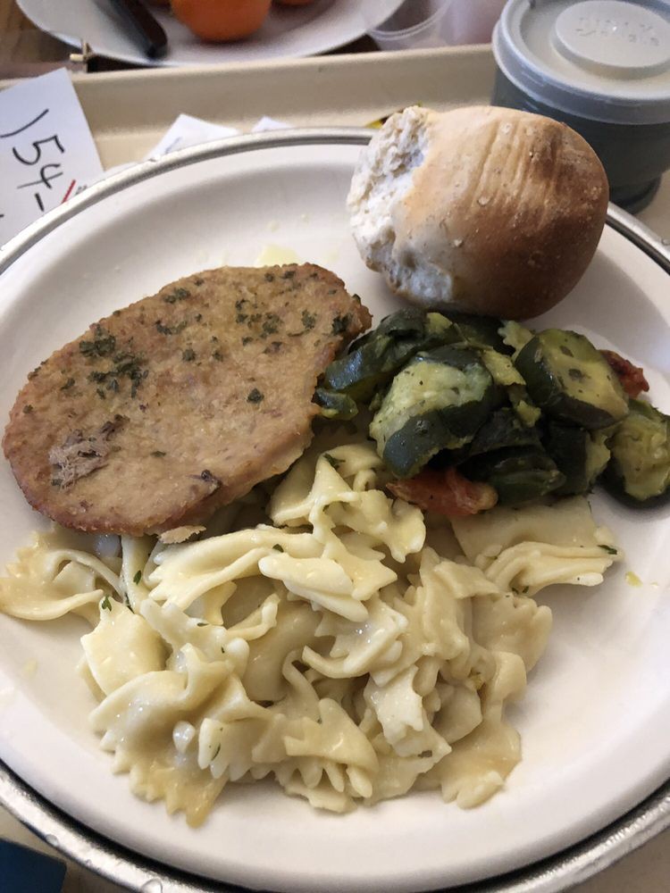 A meal featuring a slice of meat, pasta, zucchini, and a bread roll on a plate.