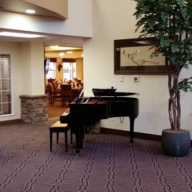 A grand piano situated in a well-decorated hallway with an artwork on the wall and a potted plant nearby.