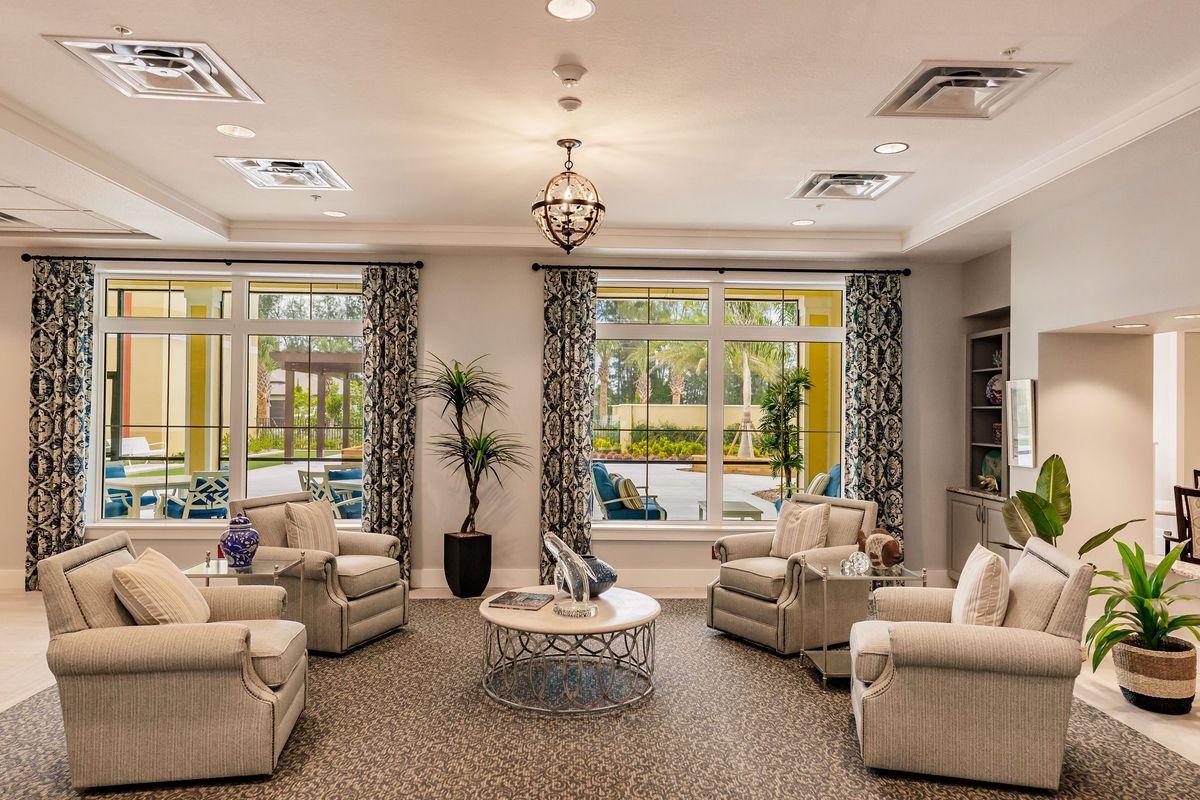 A cozy living room with comfortable seating, elegant chandelier, and large windows with patterned curtains.