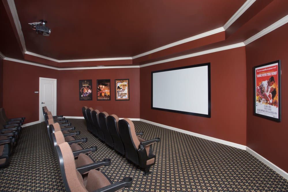 A home theater room with rows of seating, a large projector screen, and movie posters adorning the red walls.