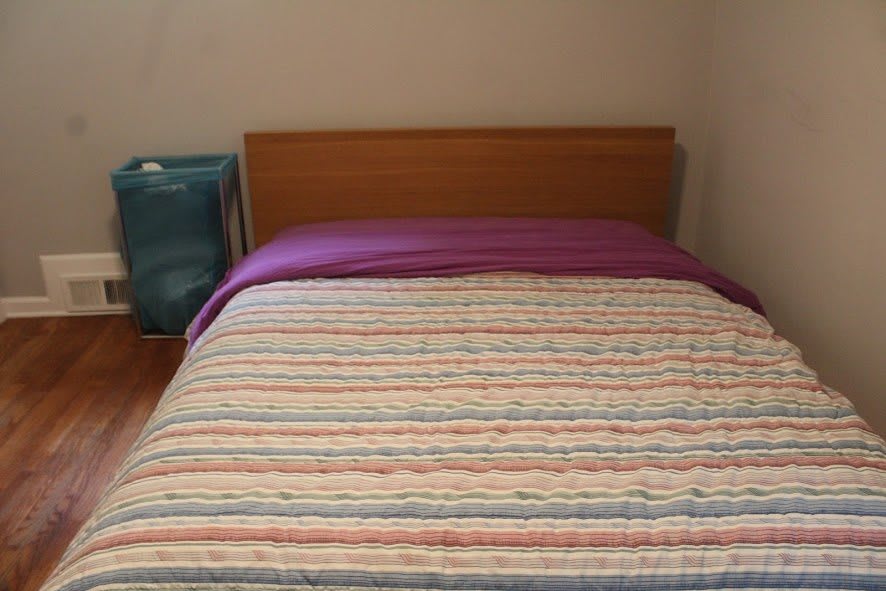 A neatly made bed with striped bedding and a wooden headboard.