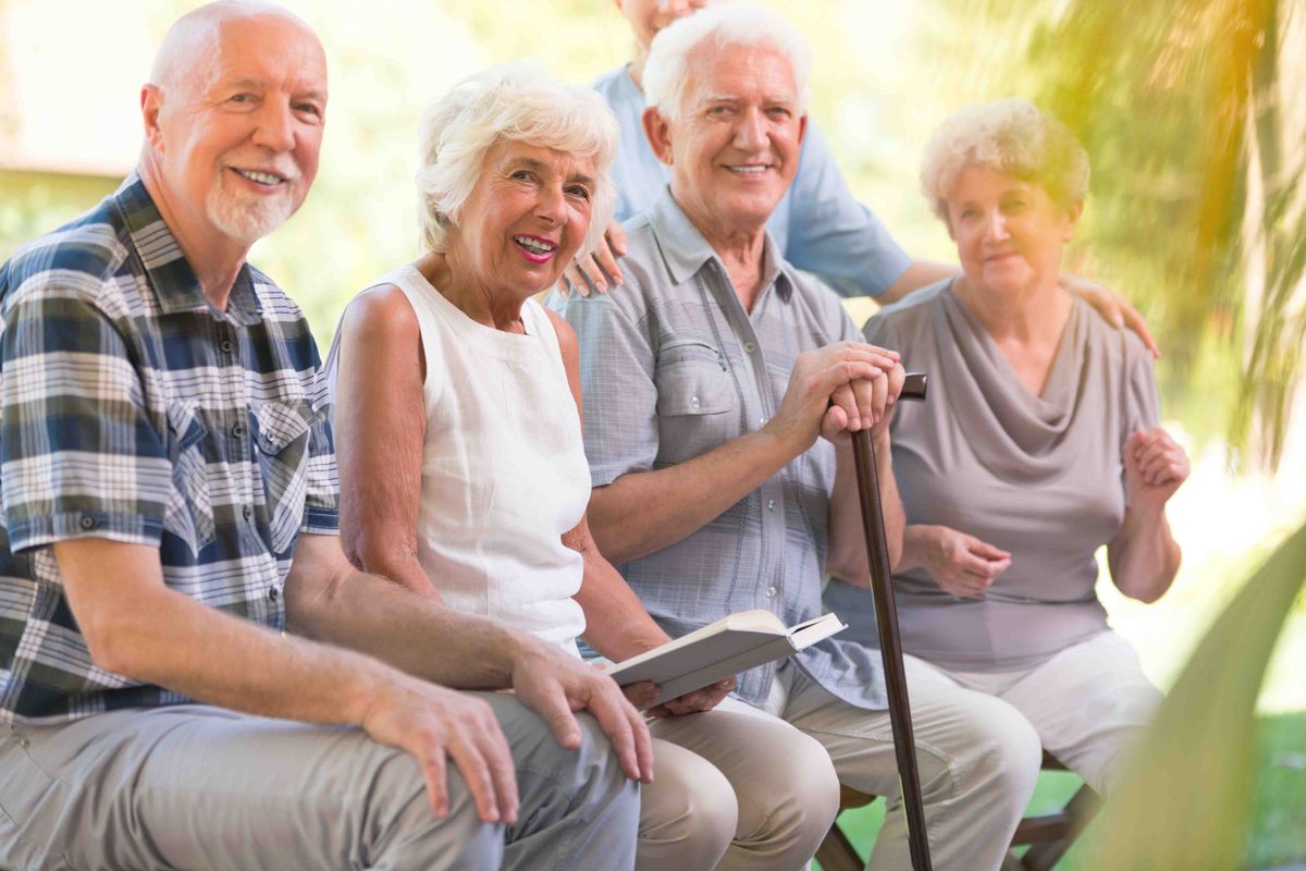 A group of elderly people sitting together outdoors, enjoying each other's company.
