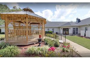 A beautifully landscaped garden featuring a wooden gazebo and vibrant flowers in front of a building.