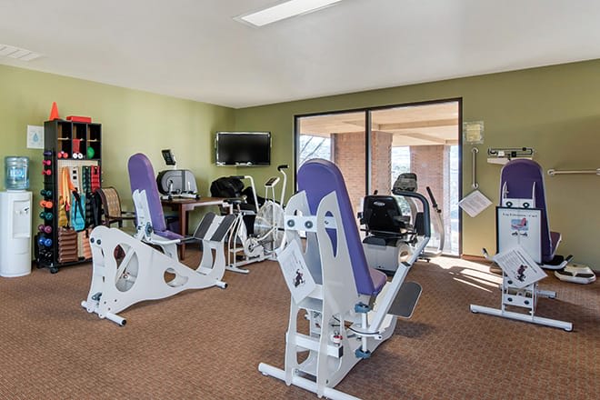 A small gym with exercise equipment, including workout machines and a TV.