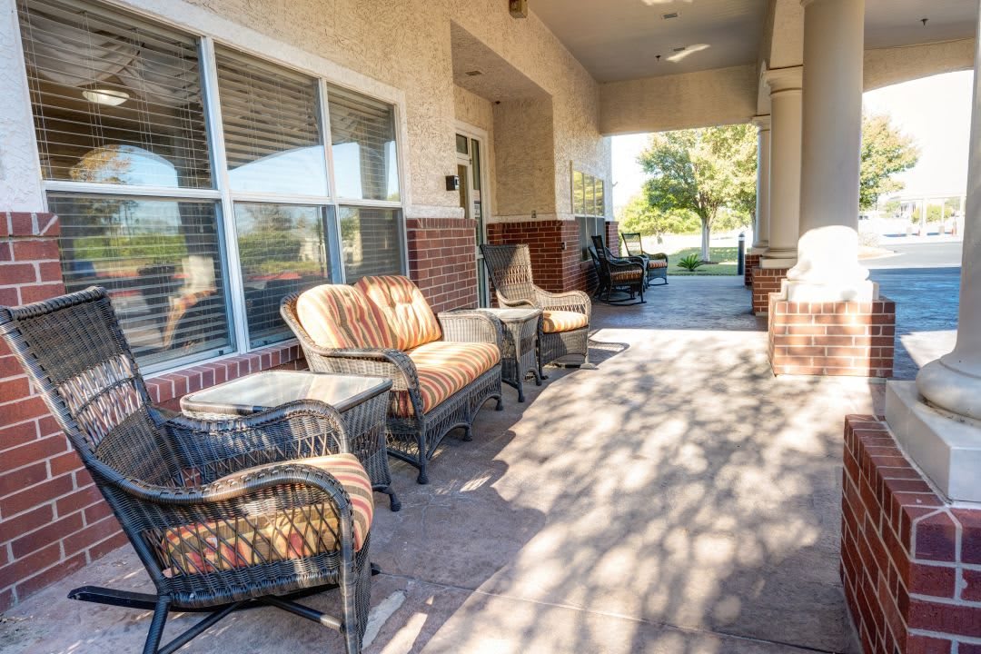 A cozy outdoor patio with wicker furniture and cushions, bathed in sunlight.