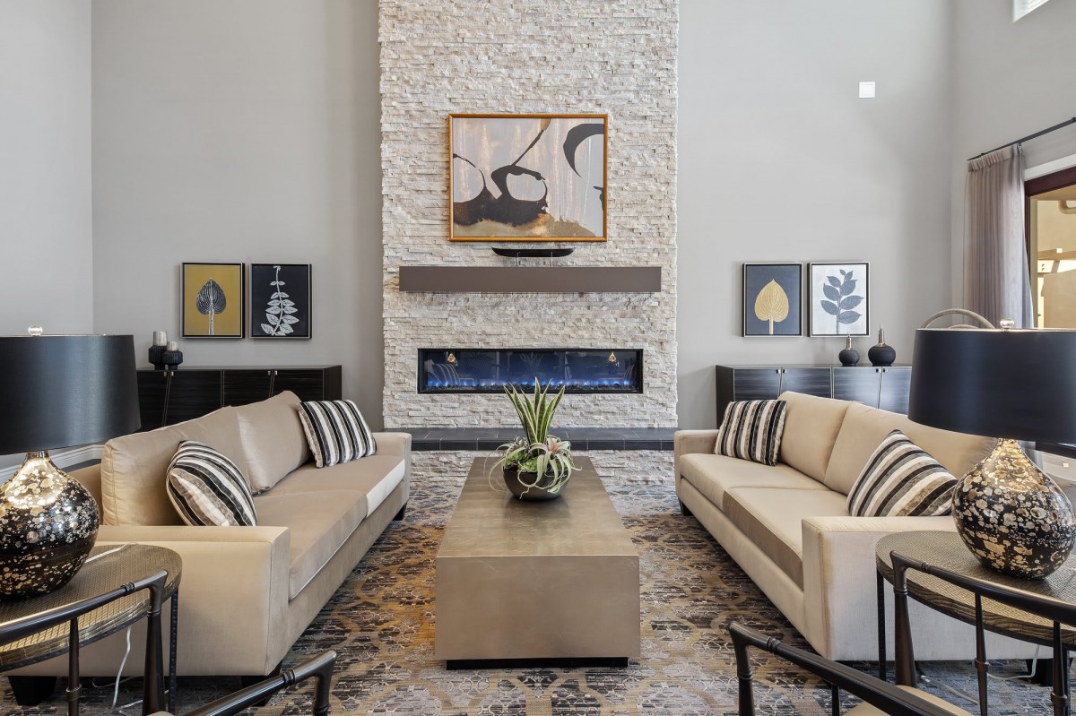 A modern living room with two beige sofas facing each other, a central coffee table, and a stylish fireplace adorned with artwork.