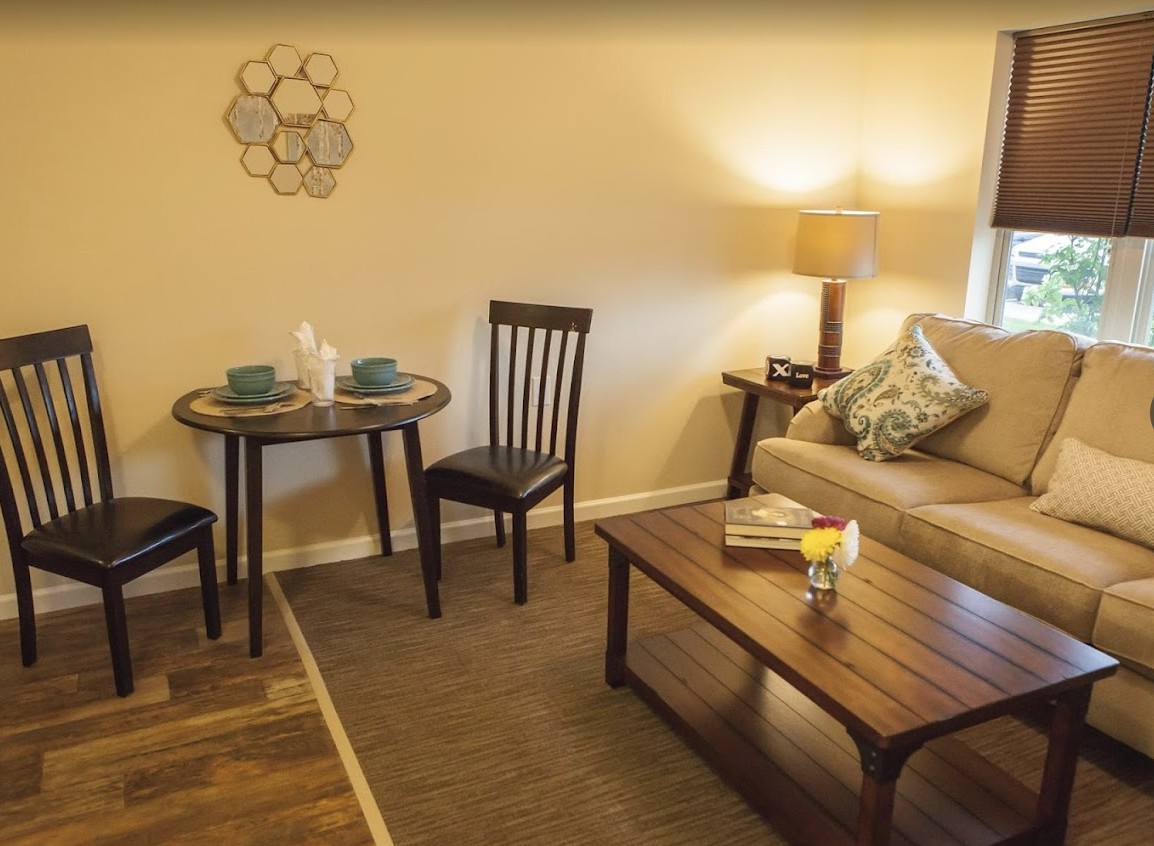 A cozy living room with a small dining table, chairs, a sofa, and a warm lamp.