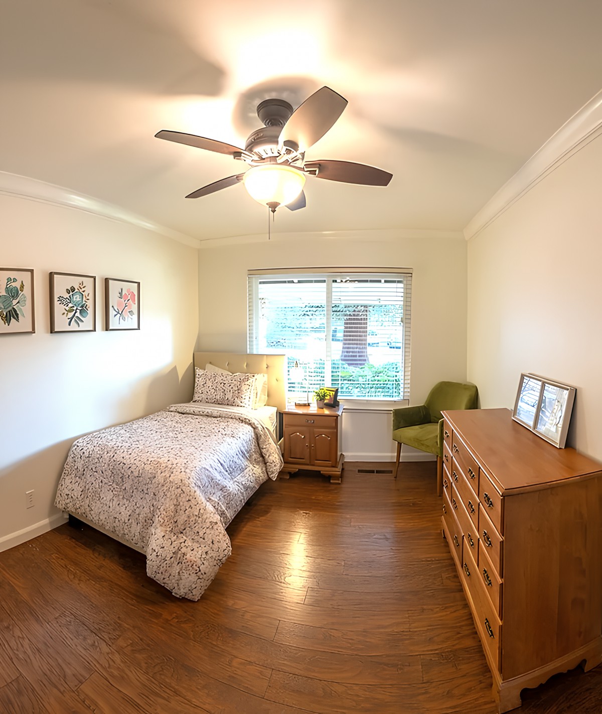 A cozy, minimalist bedroom featuring a single bed, wooden dresser, and a bright window.