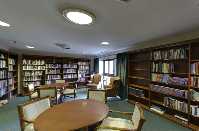 A cozy library room with bookshelves, tables, and chairs for reading.
