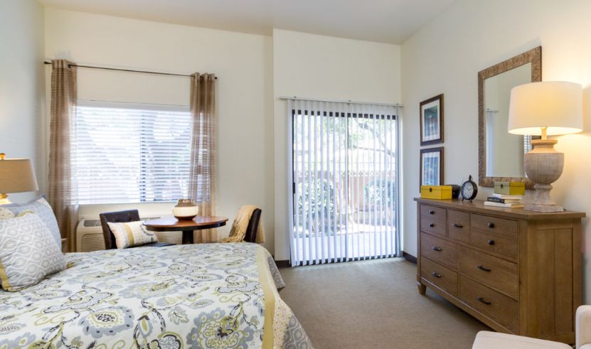 A cozy bedroom with a bed, dresser, and large windows letting in natural light.