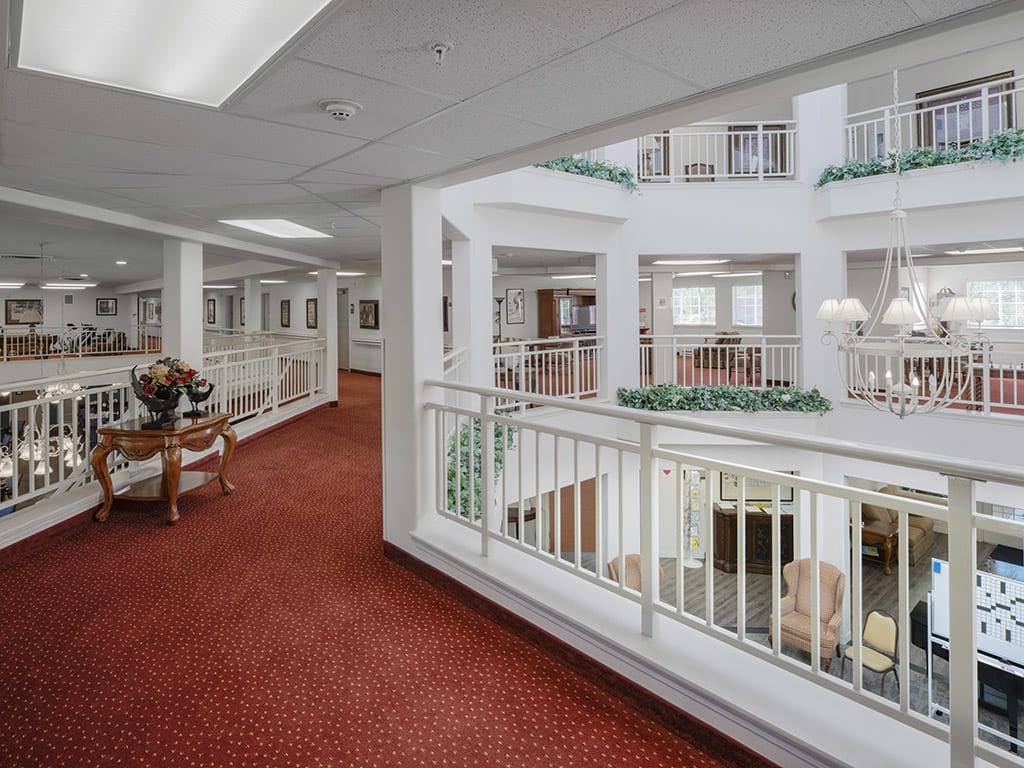 A spacious modern hallway overlooking an atrium with white railings and red carpeting.
