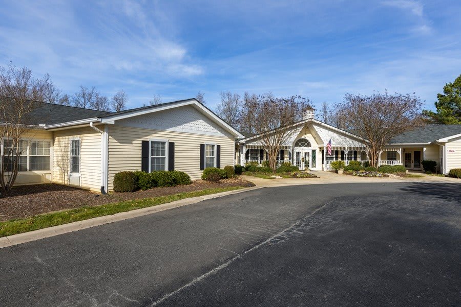 A residential building with a driveway surrounded by trees under a blue sky.