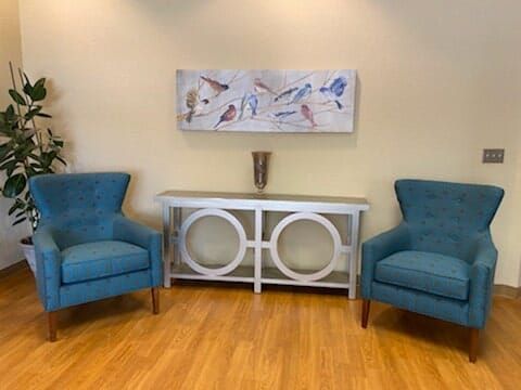 A stylish living room with two blue armchairs and a white console table beneath abstract artwork.