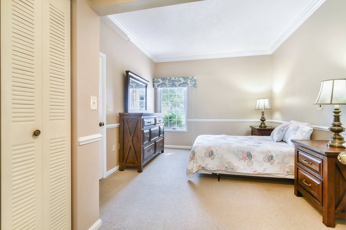 A cozy bedroom with a bed, dresser, and lamp by the window.