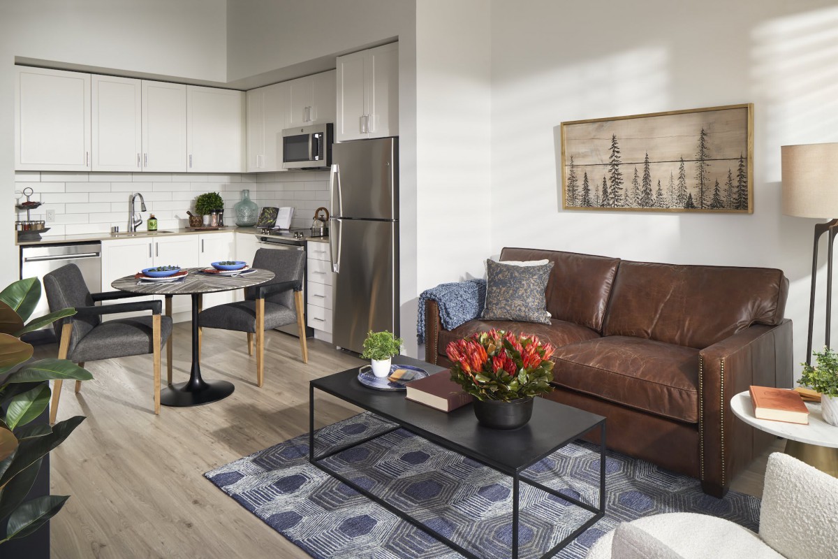A modern apartment featuring a cozy living room with a brown leather sofa and a stylish kitchen in the background.