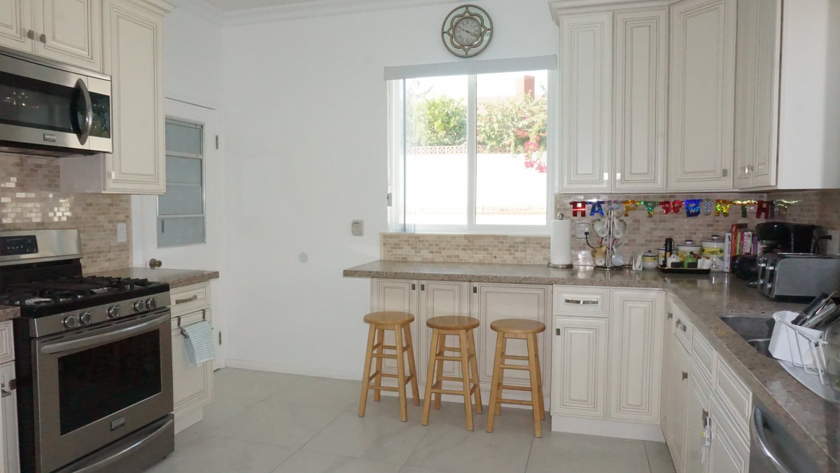A bright kitchen interior featuring white cabinets, a window, and three wooden counter stools.