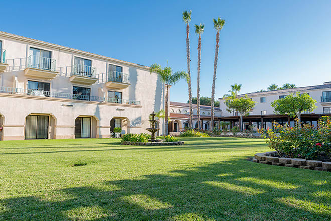 A hotel with a lush garden and palm trees on a sunny day.