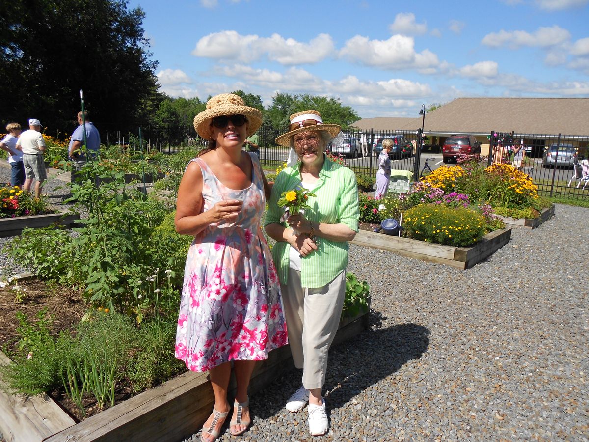 Two women enjoying a sunny day in the garden, wearing hats and holding flowers.