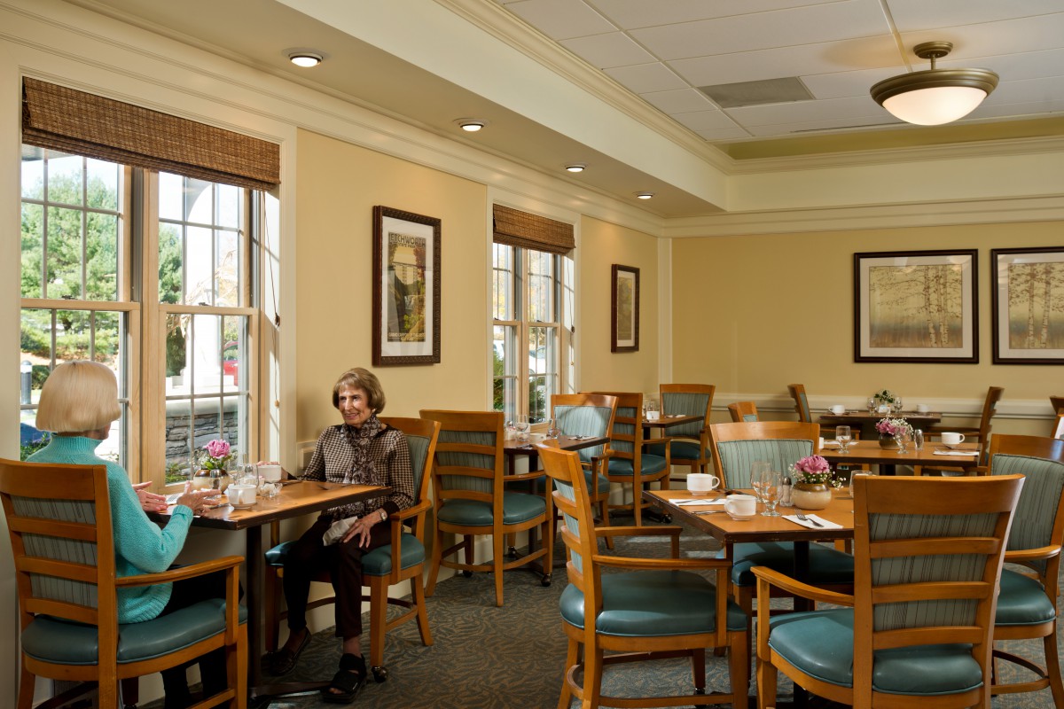 An inviting dining room with neatly arranged tables and chairs, softly lit by natural light from large windows.