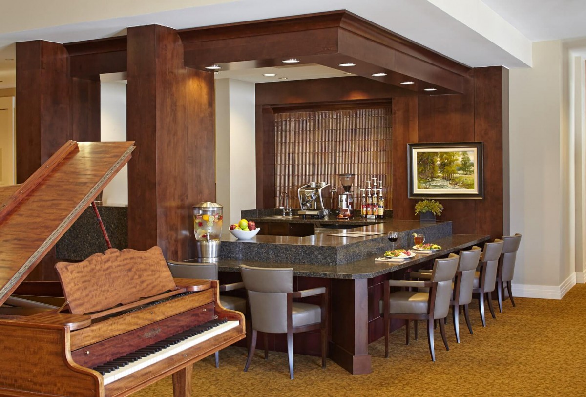 A stylish bar area with a grand piano and wooden paneling, featuring a coffee station and seating.