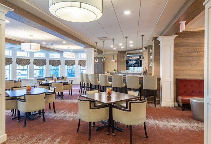 A modern restaurant interior with a bar and dining area featuring elegant seating and lighting.