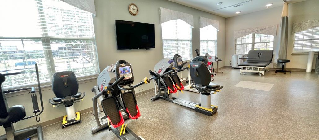 A well-lit gym with exercise machines and a television on the wall.