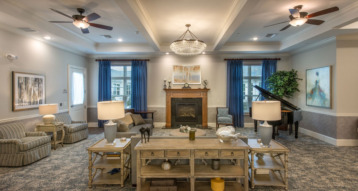 A cozy living room featuring a central fireplace, elegant chandelier, and stylish furniture with blue curtains framing large windows.