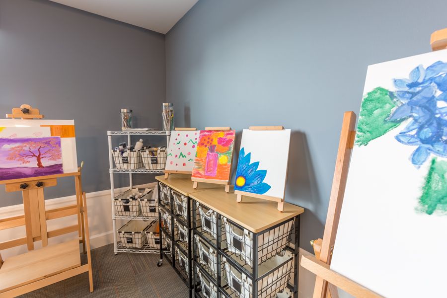A cozy art studio with vibrant paintings displayed on easels and shelves filled with art supplies.
