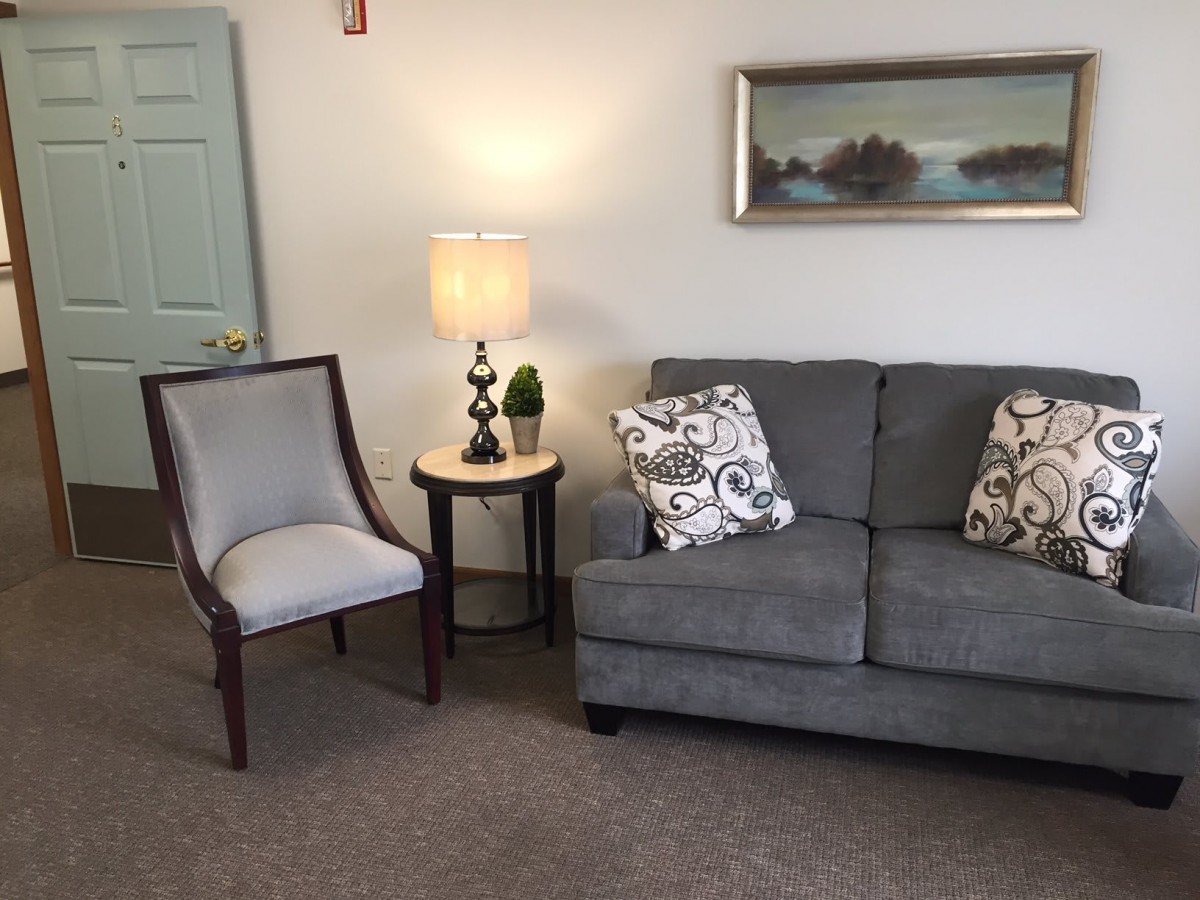 A cozy living room with a gray sofa, an accent chair, a side table with a lamp, and wall art.