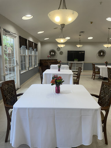 A well-lit dining area featuring neatly set tables with floral centerpieces, suitable for gatherings.