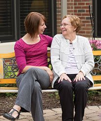 Two people sitting on a bench, engaged in a friendly conversation and smiling at each other.