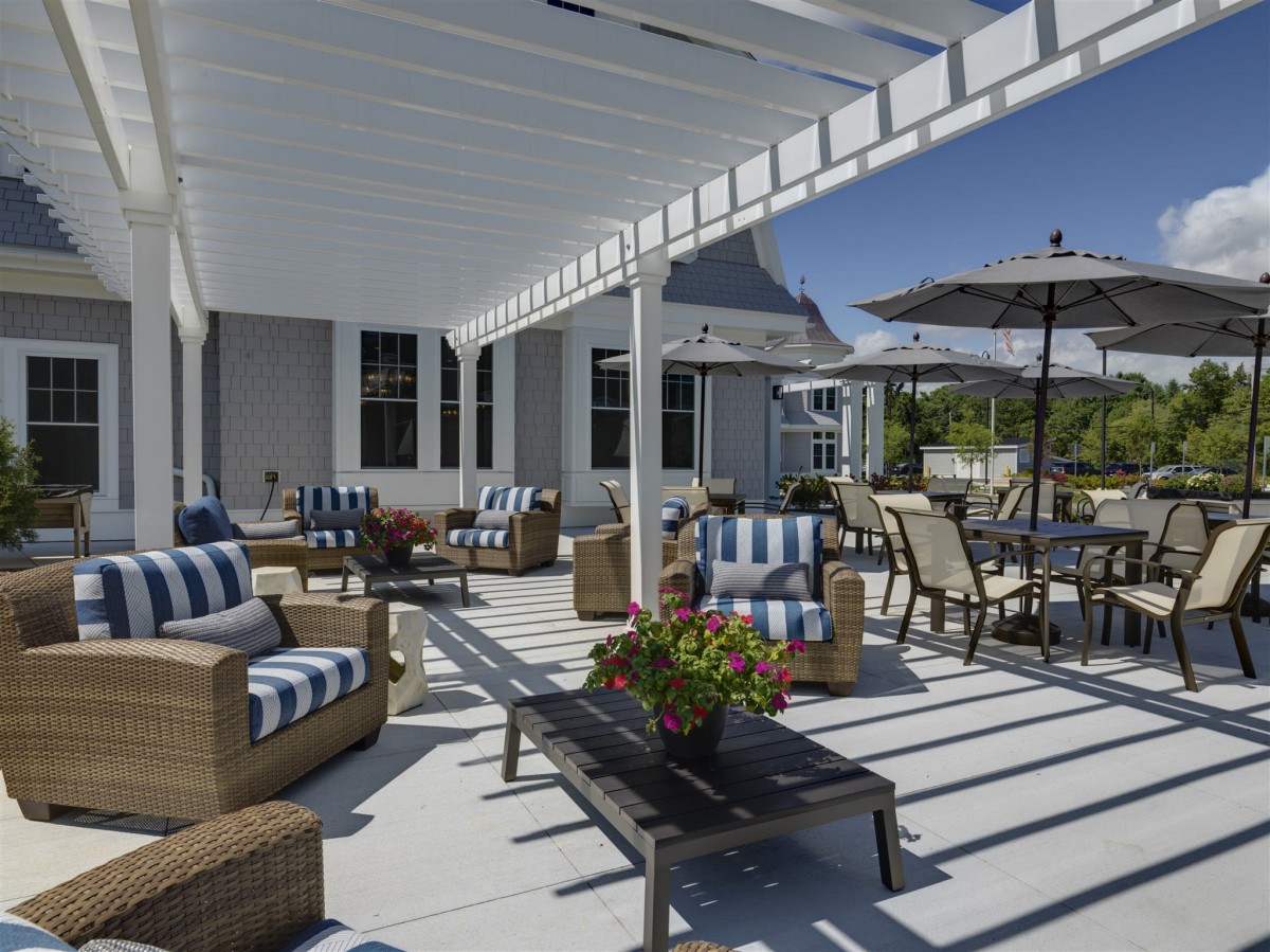 A sunny patio with comfortable wicker furniture under a pergola and an umbrella.