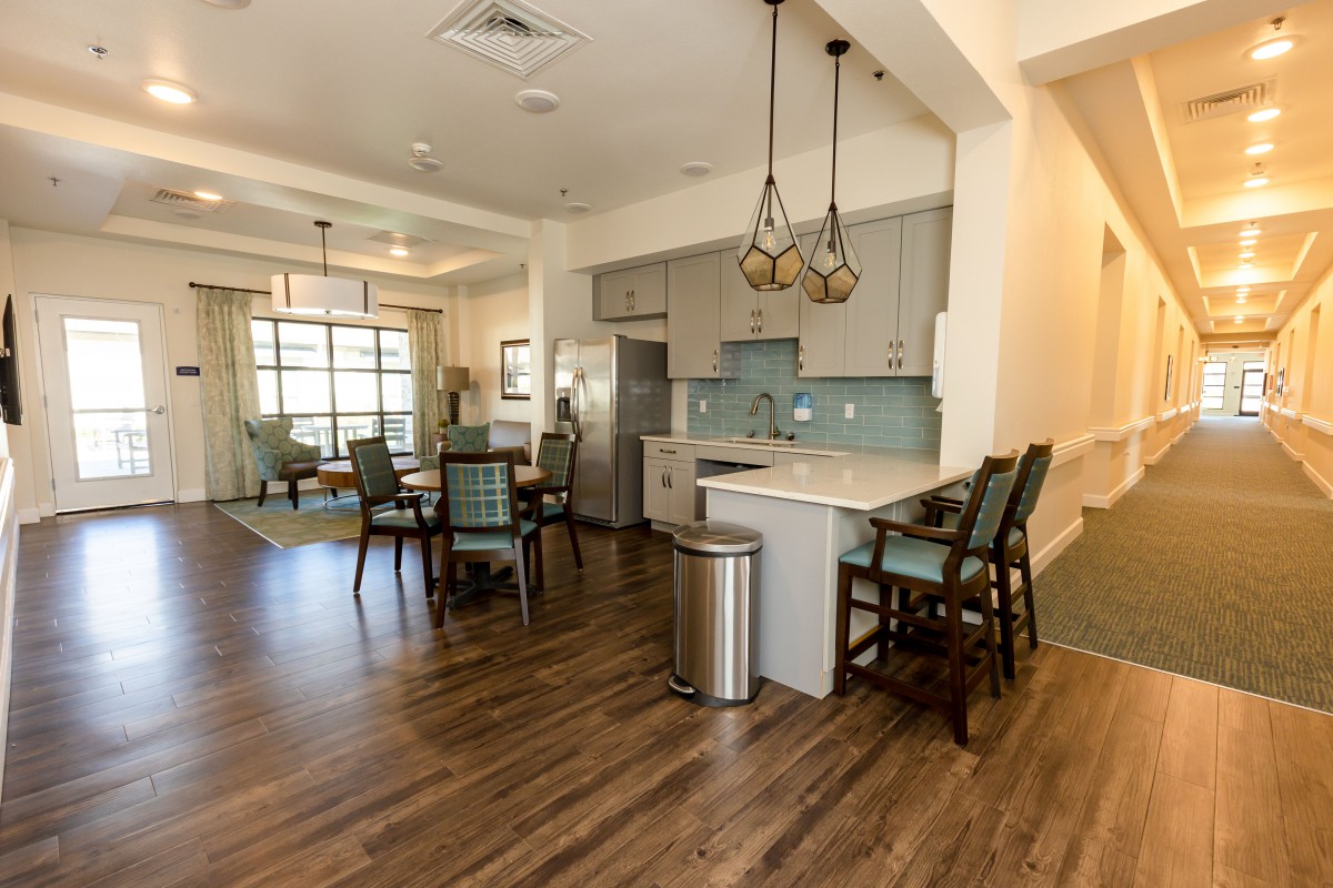 A modern open floor plan featuring a kitchen with bar seating and a dining area, highlighted by wood flooring and stylish chandeliers.