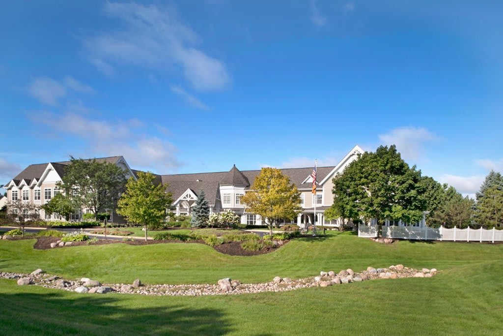 A large house surrounded by a well-maintained garden and lawn under a clear blue sky.