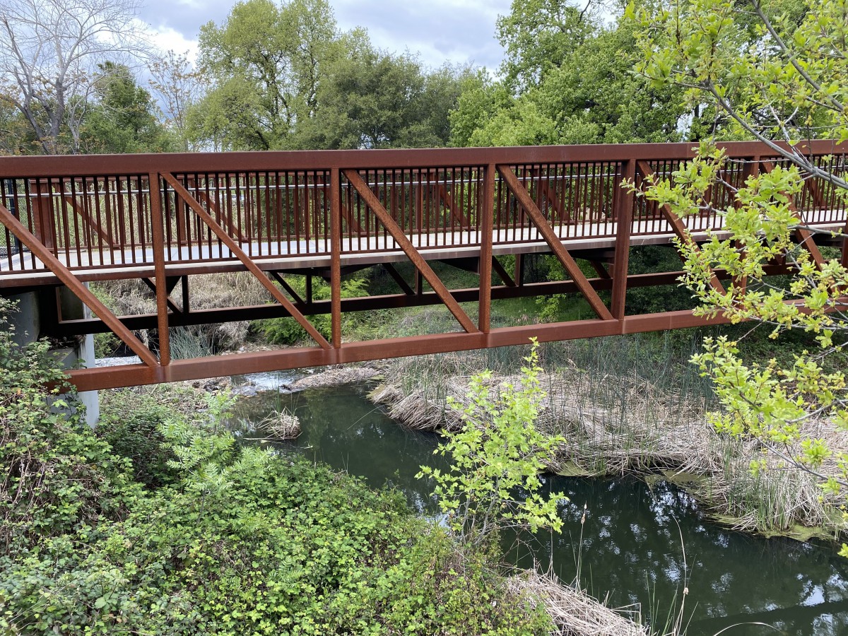 A wooden pedestrian bridge spans over a tranquil river surrounded by lush greenery.