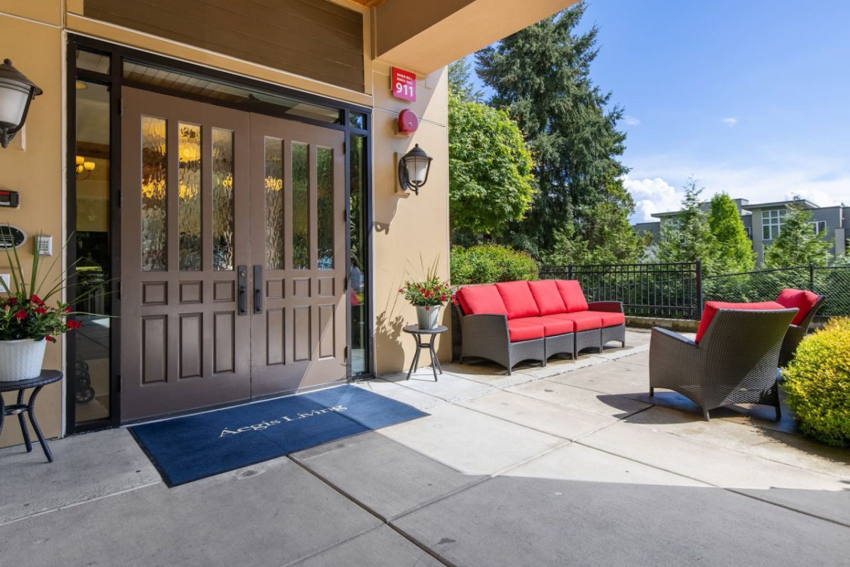 A sunny patio area with red-cushioned seating and a garden view, adjacent to an entrance.