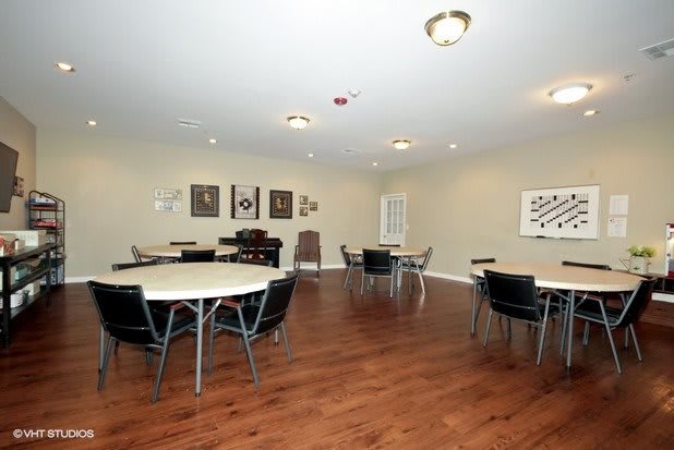 A spacious community room with tables and chairs, featuring hardwood flooring and artwork on the walls.