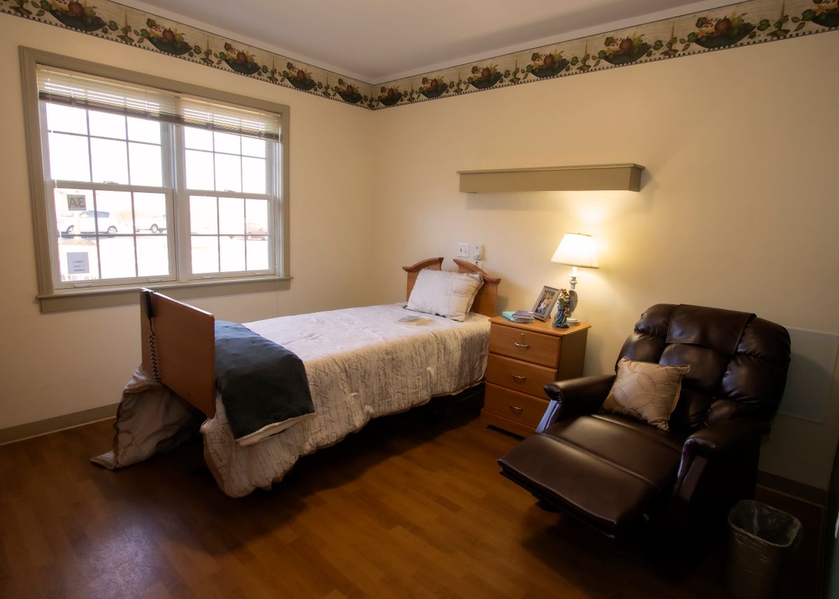 A cozy bedroom with a single bed, recliner chair, and lamp.