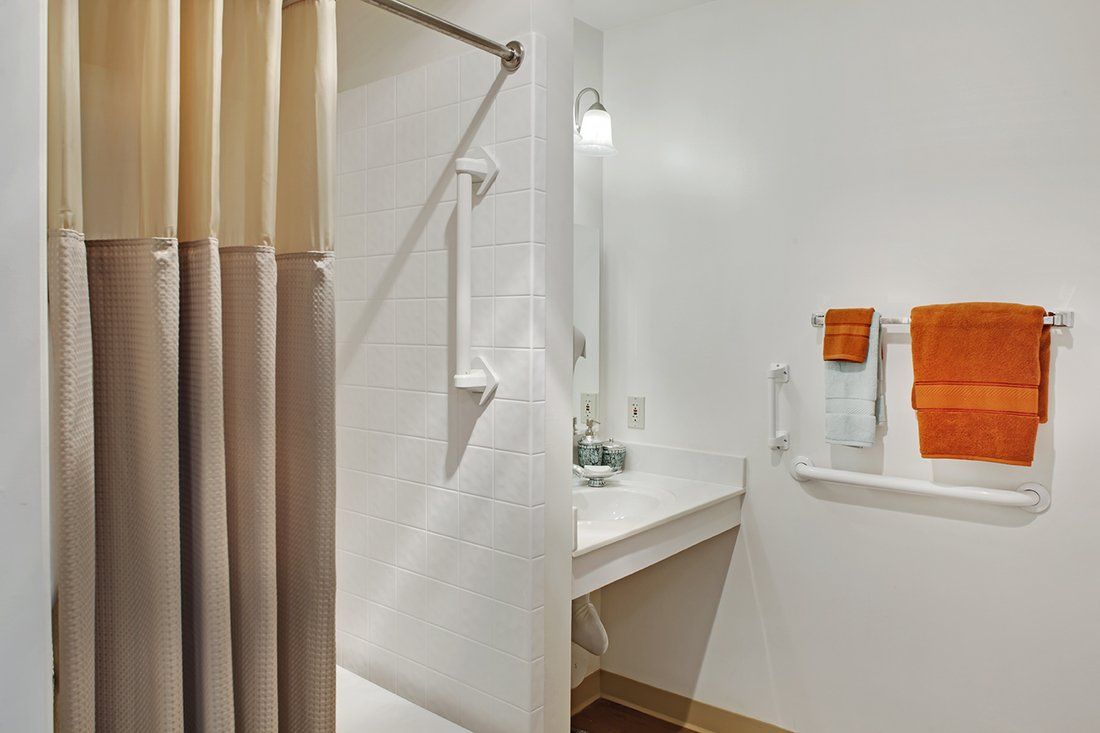 A minimalist bathroom featuring a shower, sink with a mirror, and neatly hung towels.