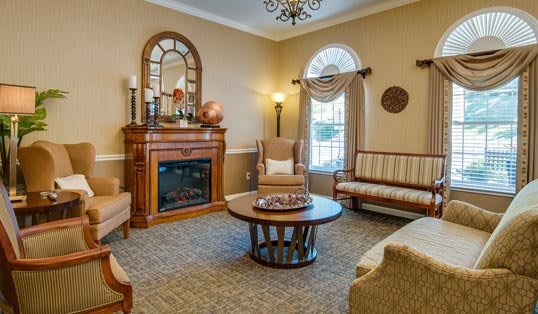 A cozy living room with a traditional design featuring a fireplace, armchair, and sofa arranged around a central coffee table.