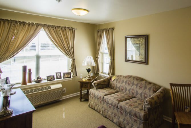 A cozy living room with a patterned sofa, curtains on windows, and a table lamp.