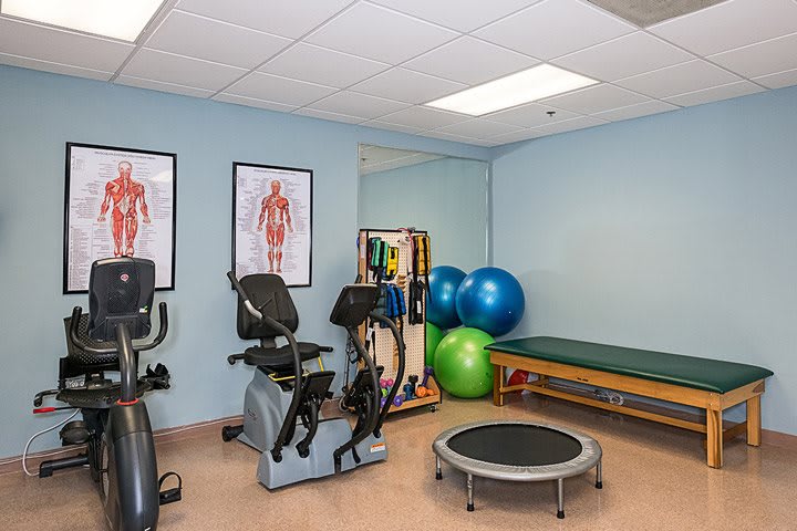 A physical therapy room equipped with exercise machines, fitness balls, and a trampoline for rehabilitation exercises.