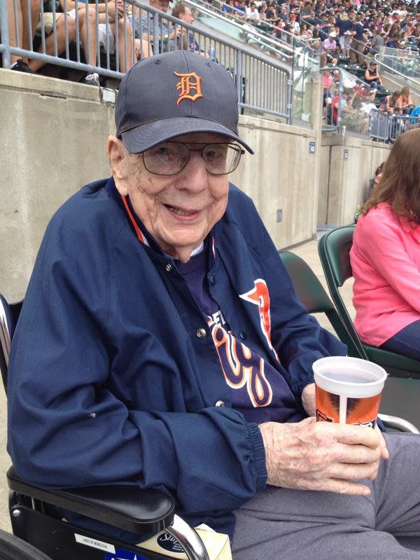 An elderly person enjoying a beverage at a baseball game.