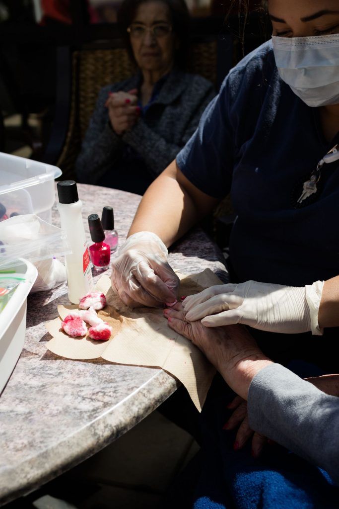 A professional performing a manicure at a nail salon, wearing gloves and applying nail polish.